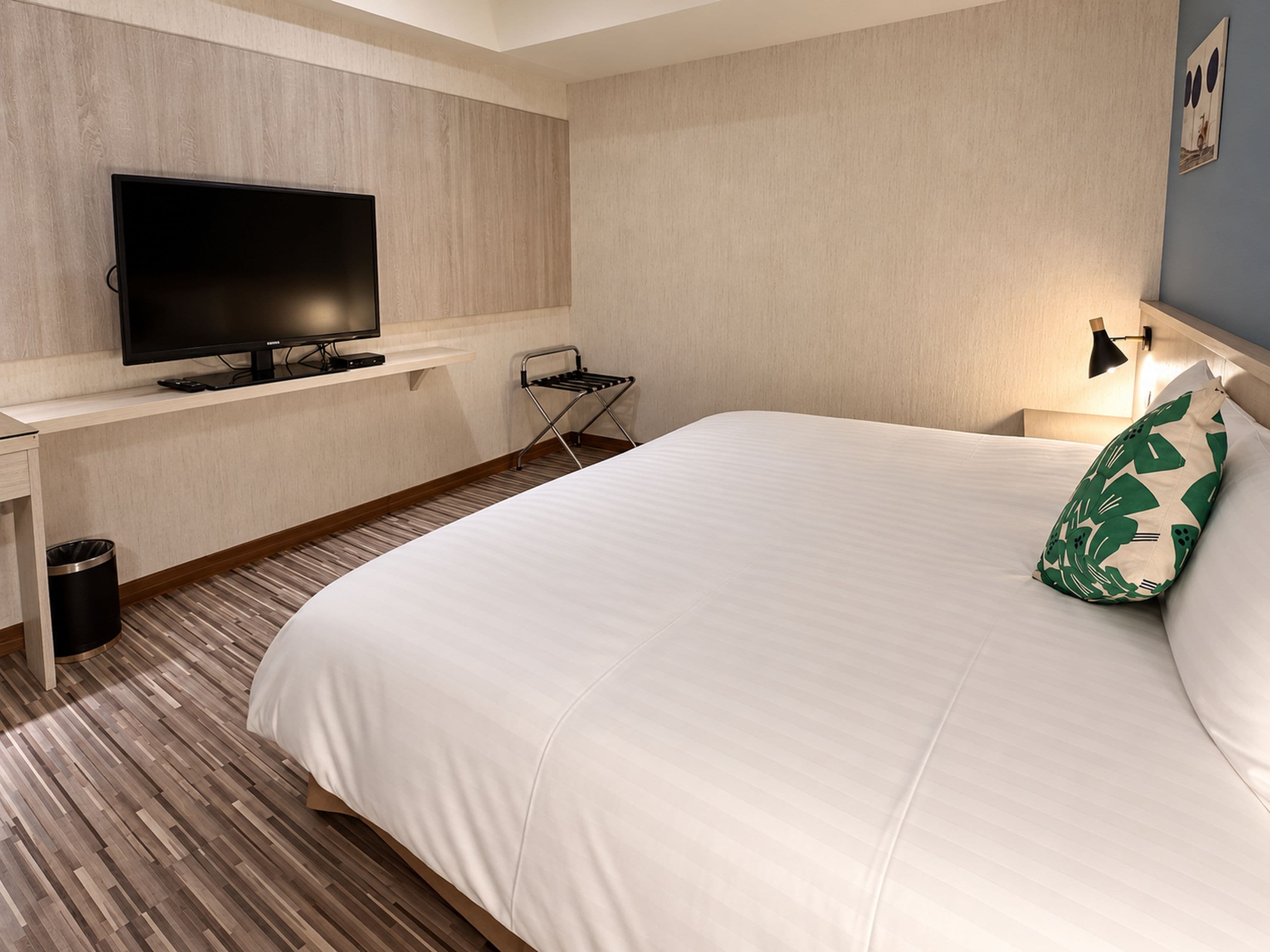 Una habitación de hotel con una cama, televisión, escritorio y lámpara.