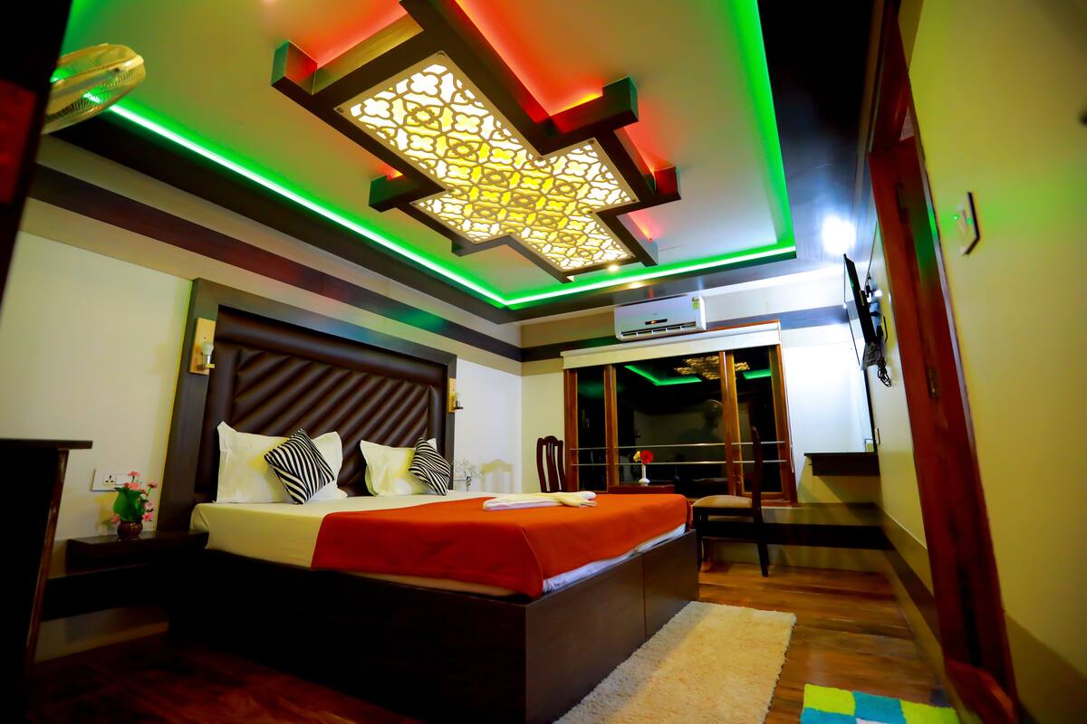 A modern bedroom with a large bed, a ceiling light fixture, and a visible air conditioning unit.