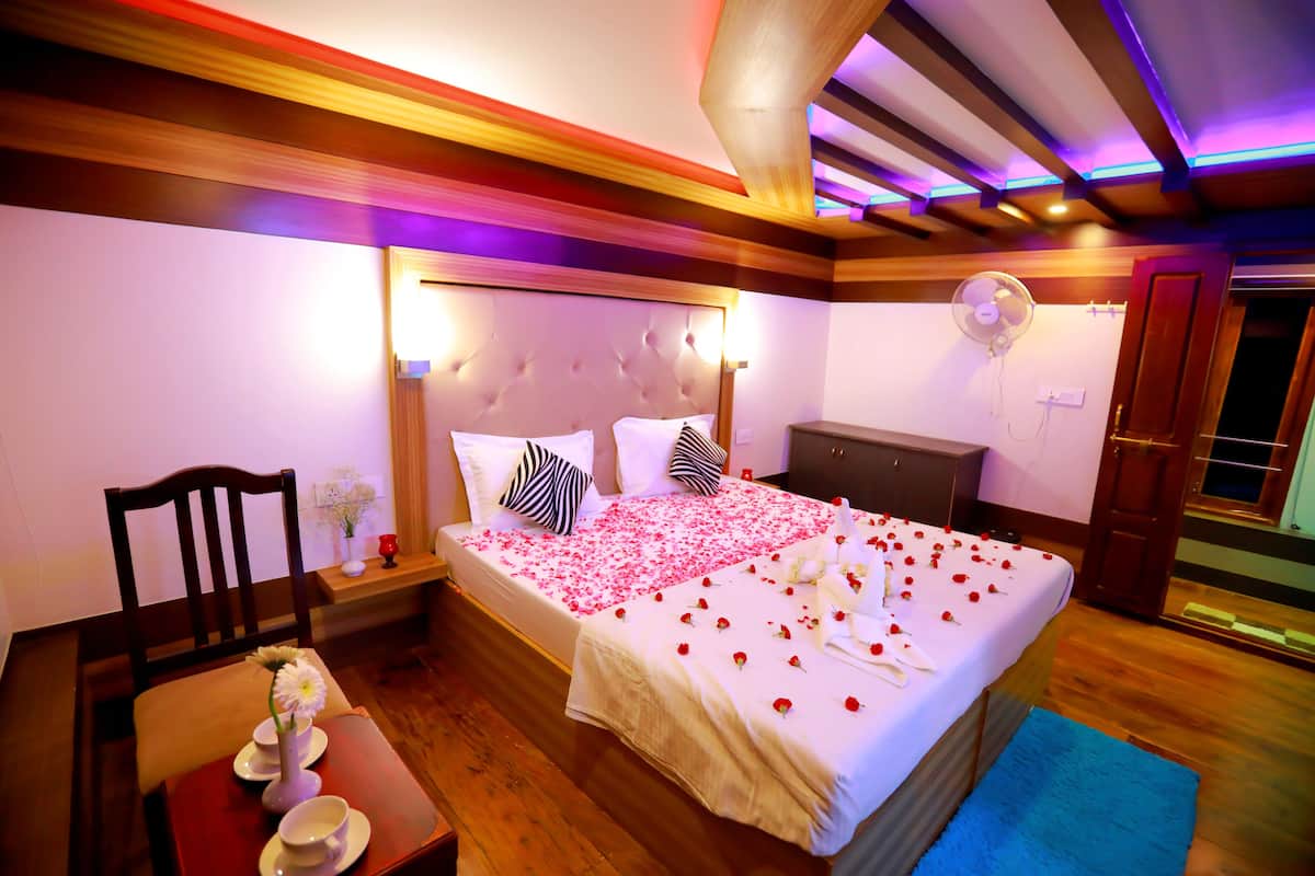 A hotel room with a bed, wooden furniture, a fan, and a blue rug.