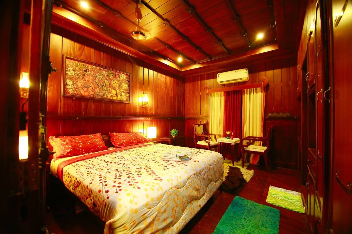 A cozy room with a large bed, wooden walls, a ceiling fan, and a small table with a chair.
