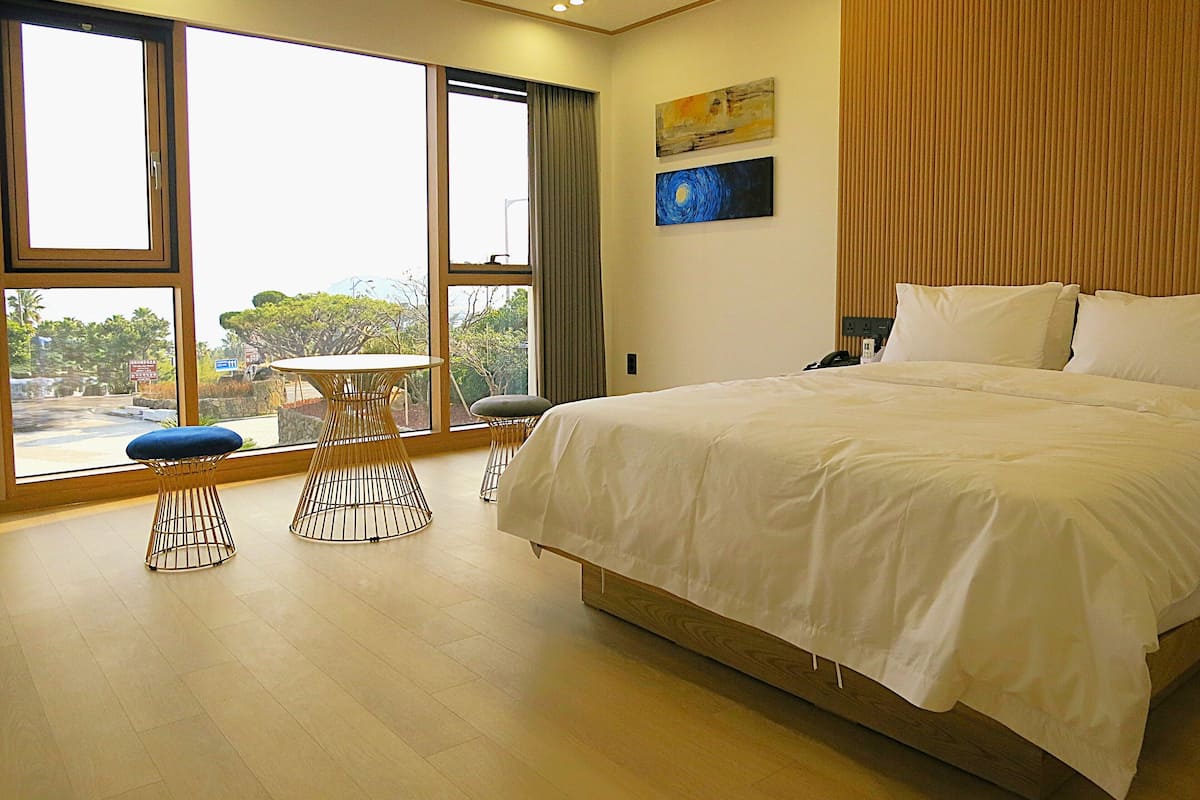 Un hotel moderno con una cama grande, una mesita redonda pequeña y vistas al exterior a través de amplios ventanales.