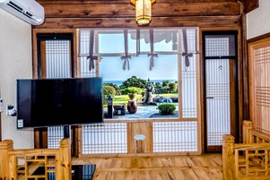 Una habitación tradicional japonesa con suelo de tatami, televisión y vistas a un jardín a través de paneles shoji.