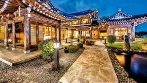 Un edificio tradicional japonés con estructuras de madera y tejados de tejas, que presenta un sendero de piedra y un pequeño jardín.