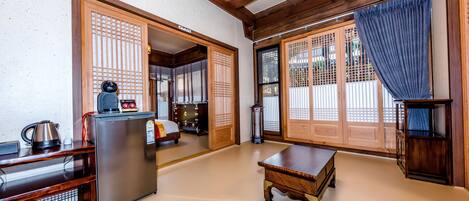 Una stanza tradizionale giapponese con pavimento in tatami, un tavolo di legno, un frigorifero e porte scorrevoli con paraventi.