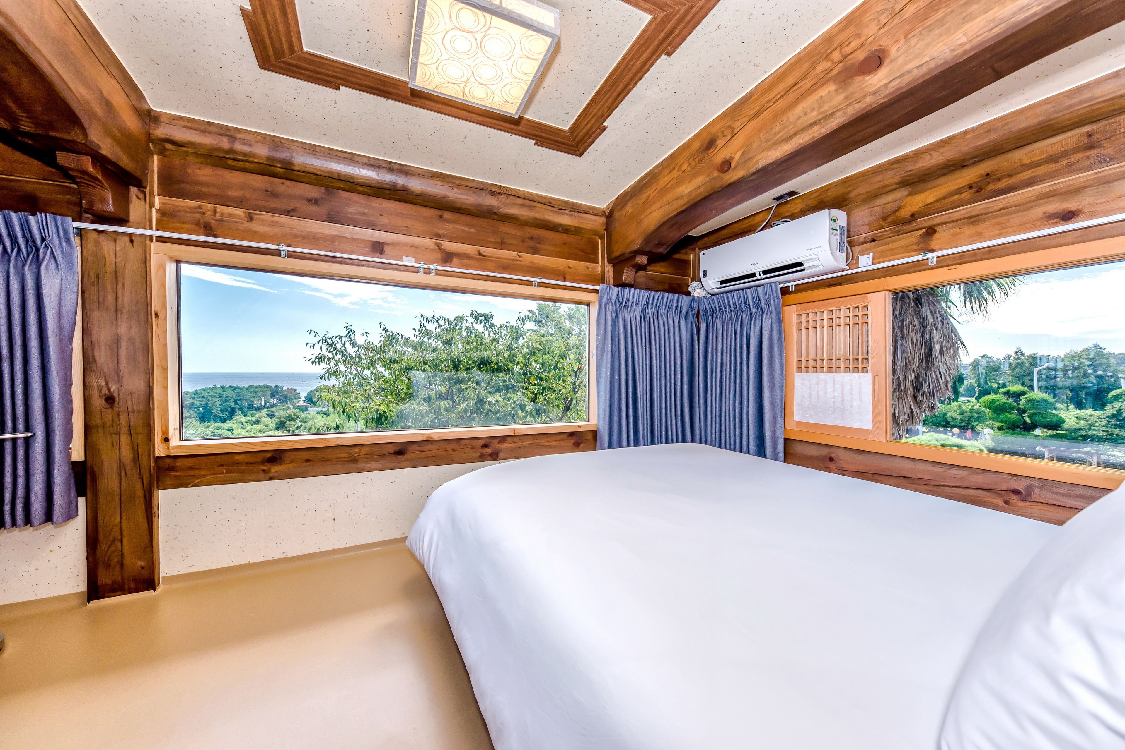 A bedroom with a large window, wooden ceiling beams, and an air conditioning unit.