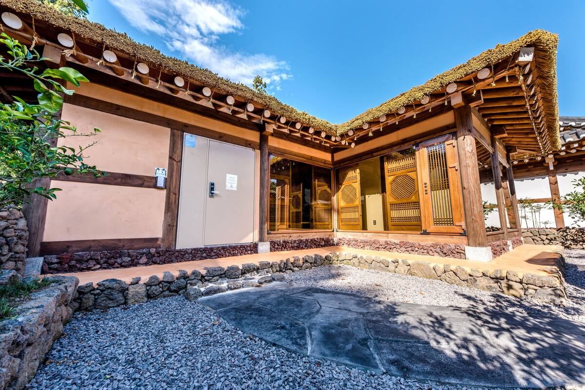 Un edificio japonés tradicional con fachada de madera, tejado de paja y un sendero de piedra que lleva a la entrada.