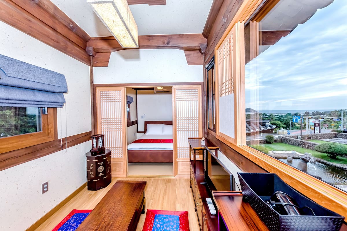 Una habitación tradicional japonesa con suelo de tatami, una cama con una manta roja, un armario de madera y un televisor.