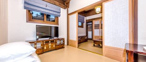 Una habitación tradicional japonesa con suelo de tatami, televisor, armario de madera y una puerta corredera que da a otra habitación.