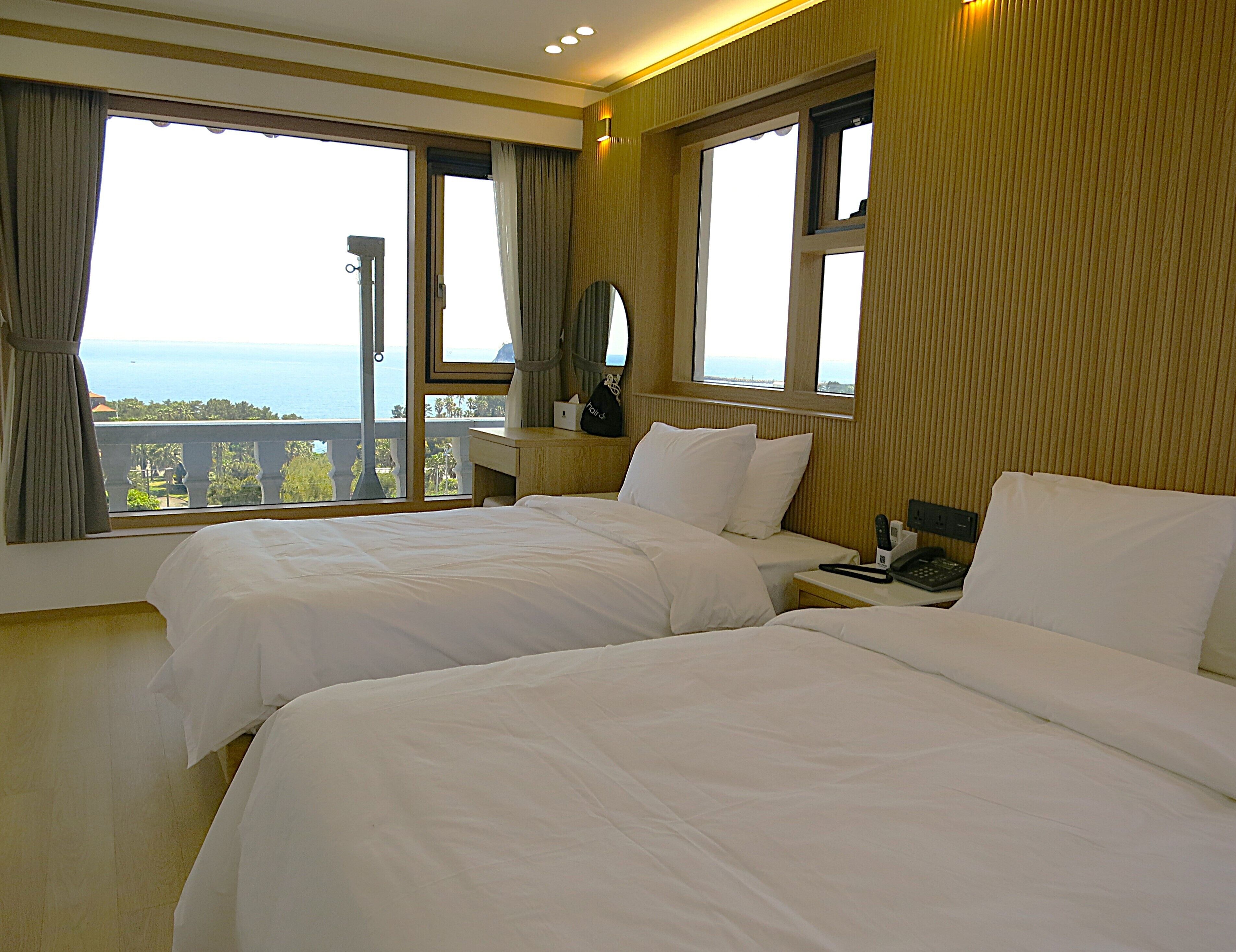 A hotel room with two beds, a bedside table with a phone, and a view of the sea.