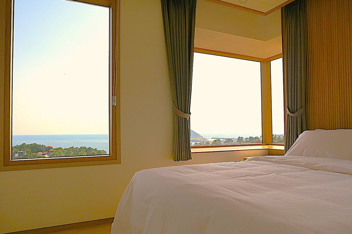 Un dormitorio con un ventanal grande, una cama y cortinas.