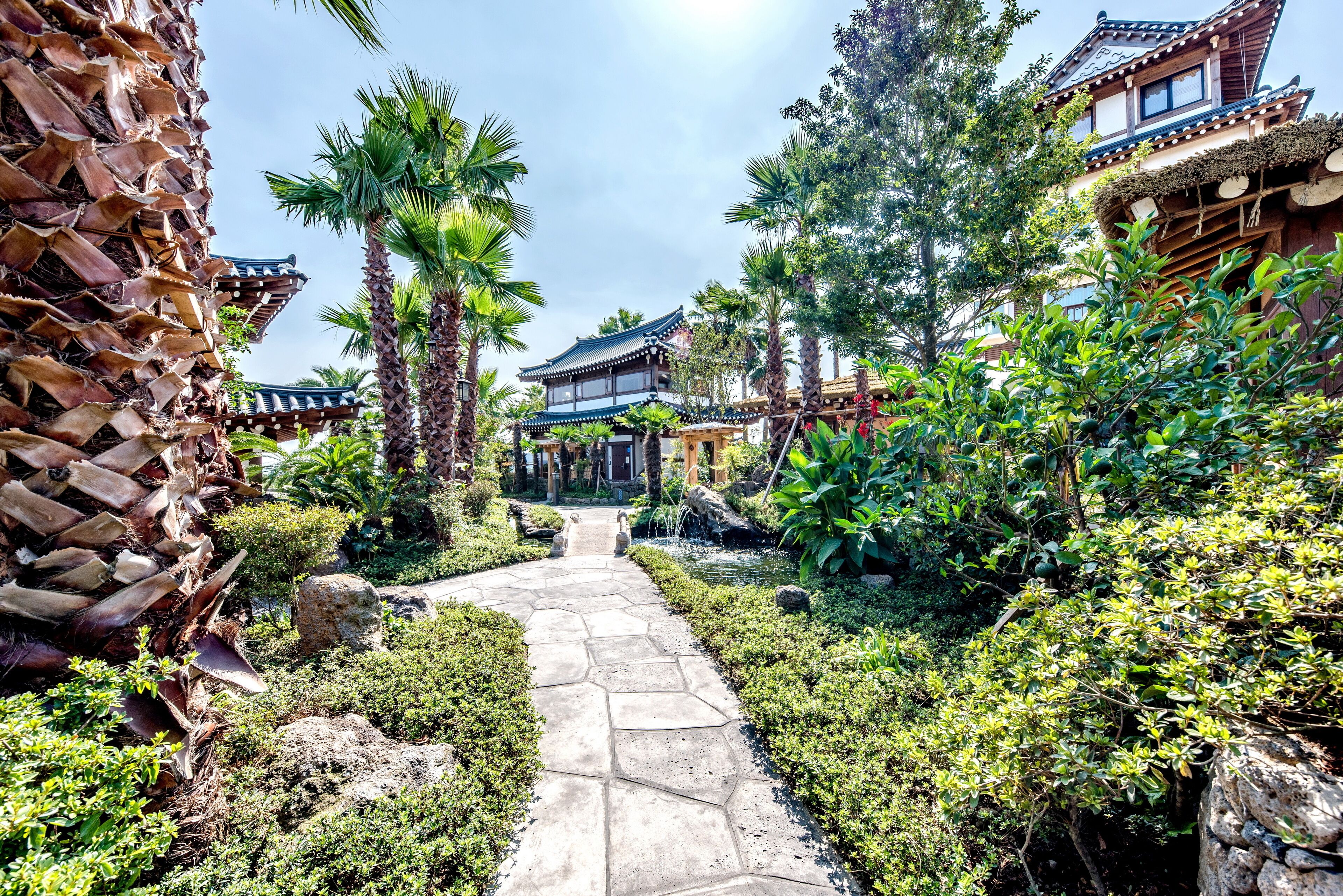A traditional Japanese garden with a stone pathway leading to a wooden building with a tiled roof.