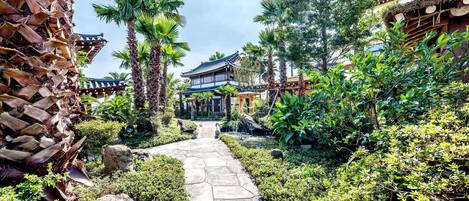 A traditional Japanese garden with a stone pathway leading to a wooden building with a tiled roof.
