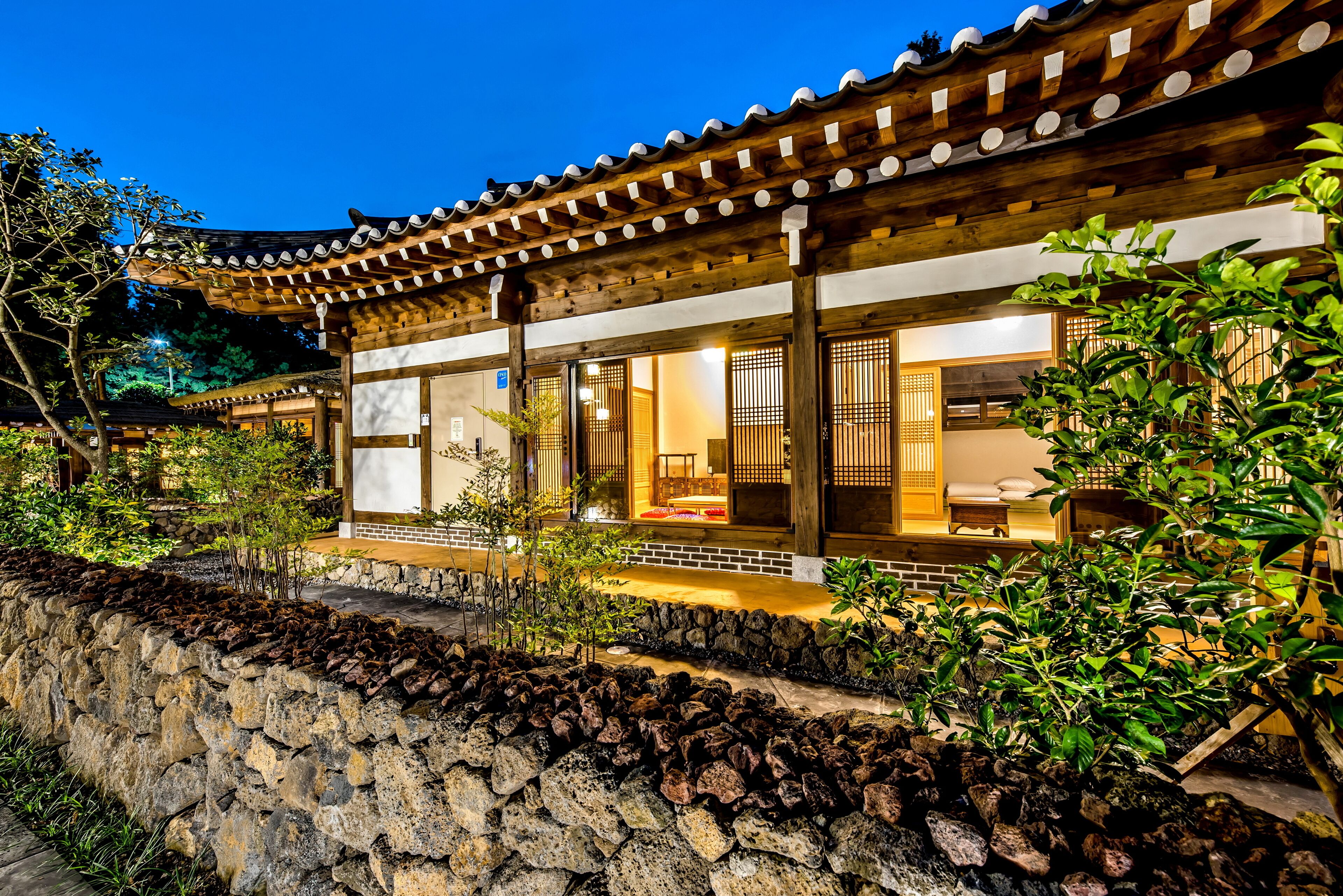A traditional building with a tiled roof and wooden beams, surrounded by greenery and a stone wall.