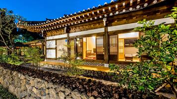 A traditional building with a tiled roof and wooden beams, surrounded by greenery and a stone wall.