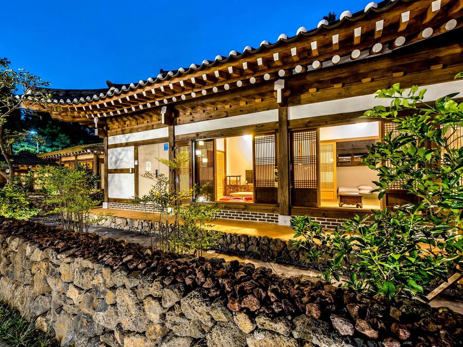 A traditional building with a tiled roof and wooden beams, surrounded by greenery and a stone wall.