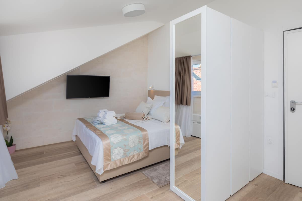 A modern hotel room with a bed, a flat-screen TV mounted on the wall, a door, and a view of the outside.
