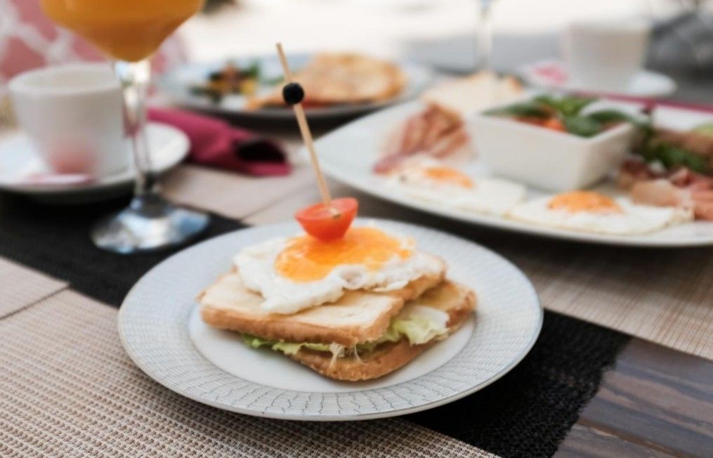 A breakfast setting with a plate of toast topped with a fried egg and a tomato, a glass of orange juice, and other dishes in the background.