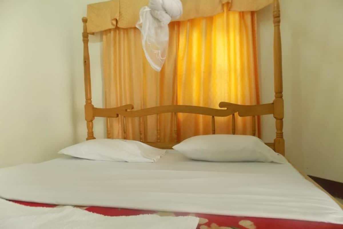 Un lit avec une tête de lit en bois, des oreillers blancs et une couvre-lit à motifs floraux rouges.