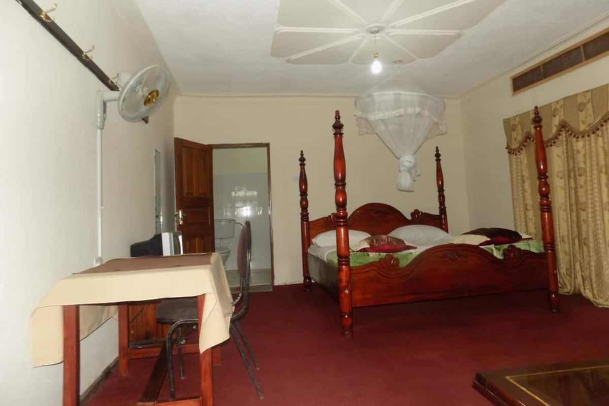 Une chambre à coucher avec un lit à baldaquin, un bureau avec une chaise, un ventilateur de plafond et une fenêtre avec des rideaux.