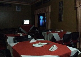 Un restaurante tenuemente iluminado con mesas cubiertas de manteles rojos, algunas con platos y cubiertos.