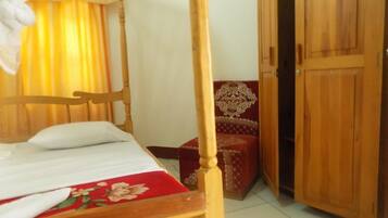A wooden bed with a headboard, a red floral bedspread, a wooden chair with a patterned cushion, and a wooden wardrobe.
