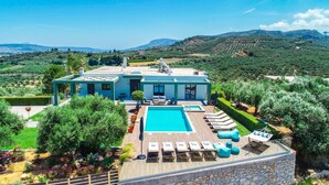 Une villa moderne dotée d’une piscine, de chaises longues et offrant une vue sur le paysage environnant.