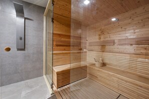 Uma sauna com divisória de vidro, bancos de madeira e zona de chuveiro moderna.
