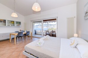 A hotel room with a bed, a desk, chairs, a balcony with a view, and a window.