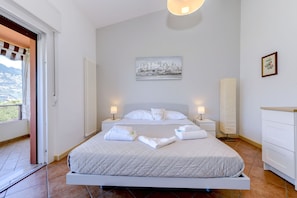 Une chambre à coucher comprenant un lit, deux tables de chevet, une commode, un radiateur, un tableau et une fenêtre avec des rideaux.