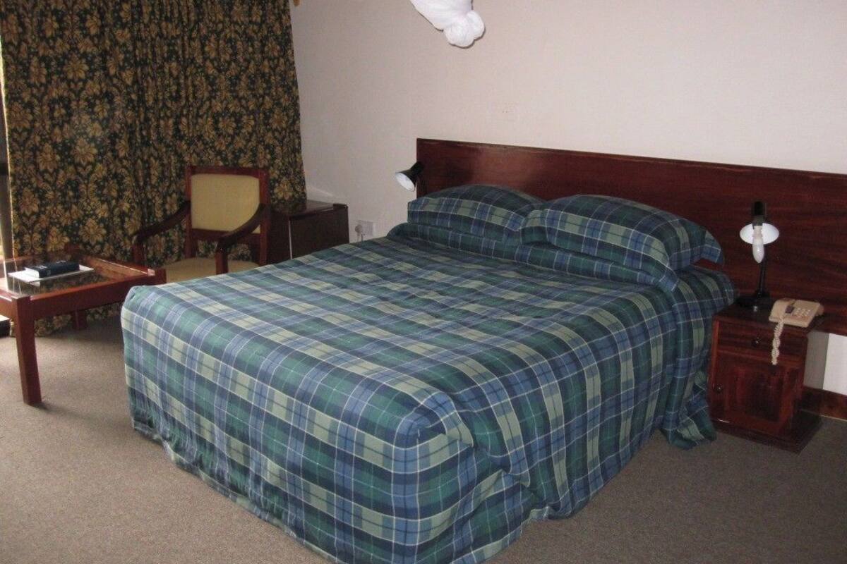 Une chambre d’hôtel standard, équipée d’un lit, d’une chaise, d’une table de chevet et d’un téléphone.