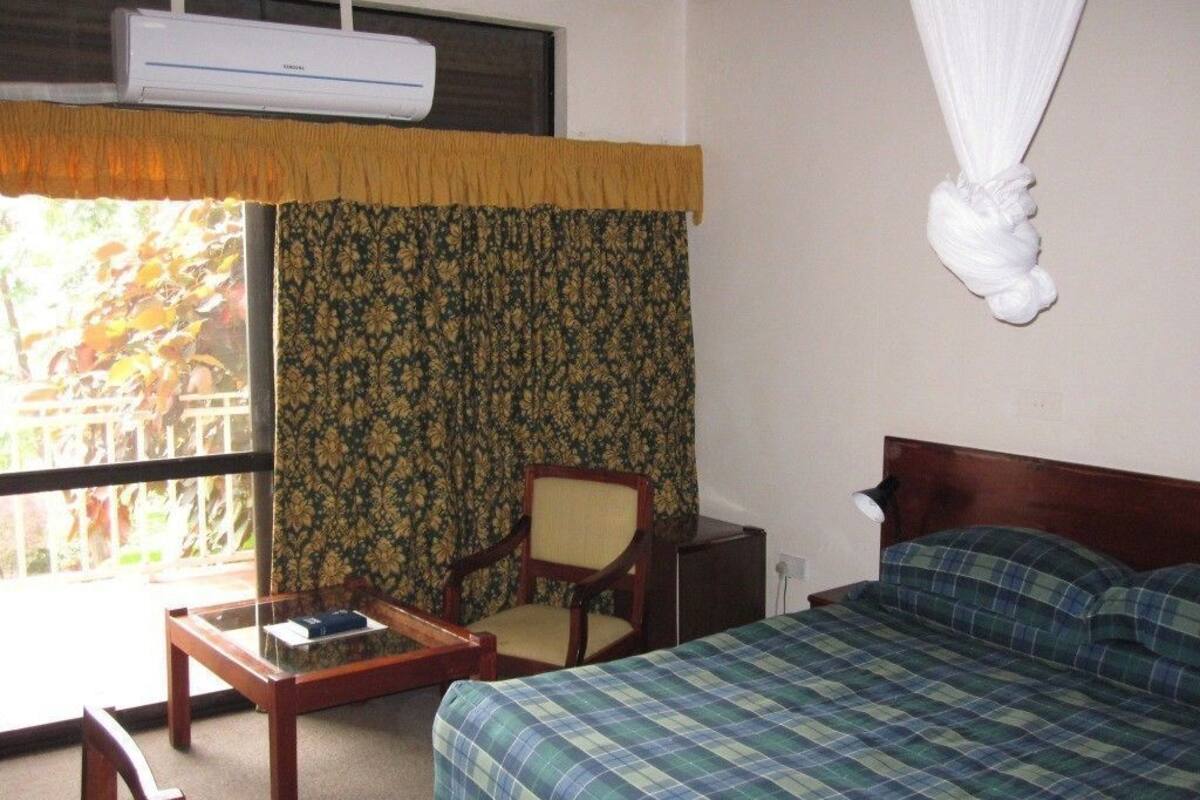 Une chambre d’hôtel comprenant un lit, une chaise, une petite table, une fenêtre avec des rideaux et un appareil de climatisation.