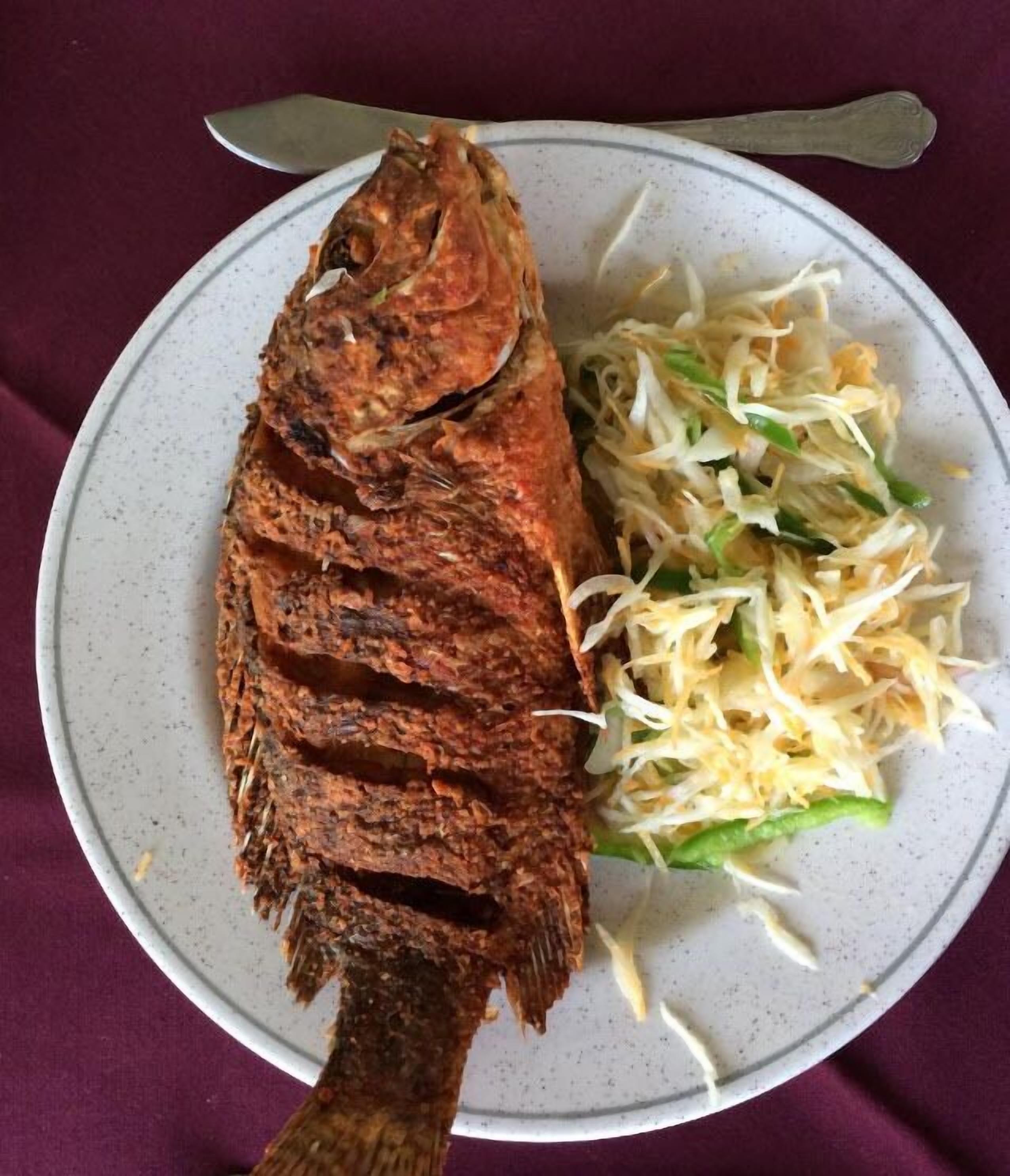 En hel, ugnsrostad fisk serverad på ett fat med strimlad grönsaksröra som tillbehör.