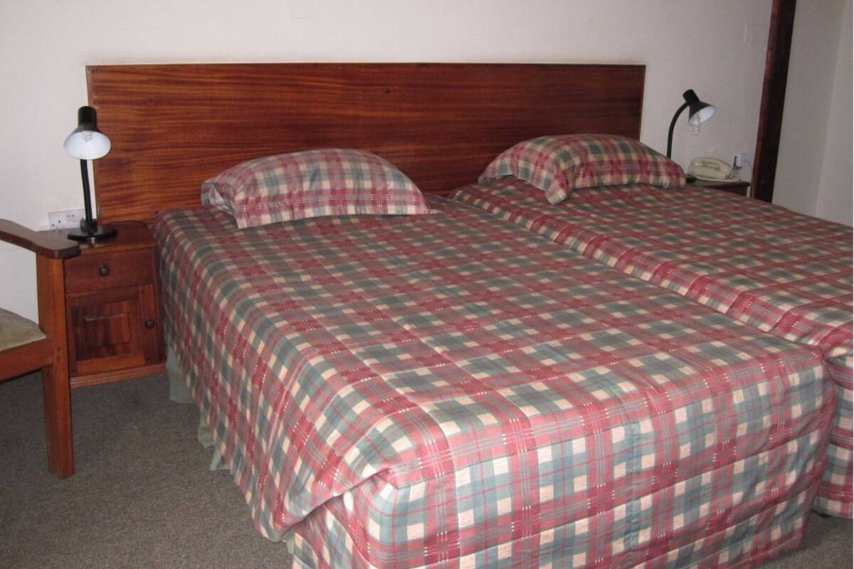 Un lit double avec une couvre-lit à carreaux, une tête de lit en bois, une table de chevet avec une lampe et un téléphone sur le côté droit.