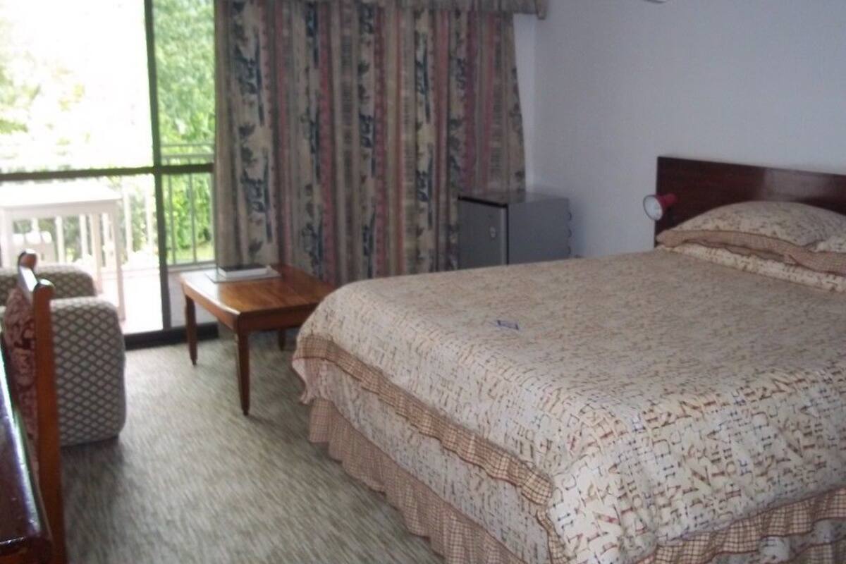 Une chambre à coucher avec un lit, une petite table, une chaise et une fenêtre avec des rideaux.