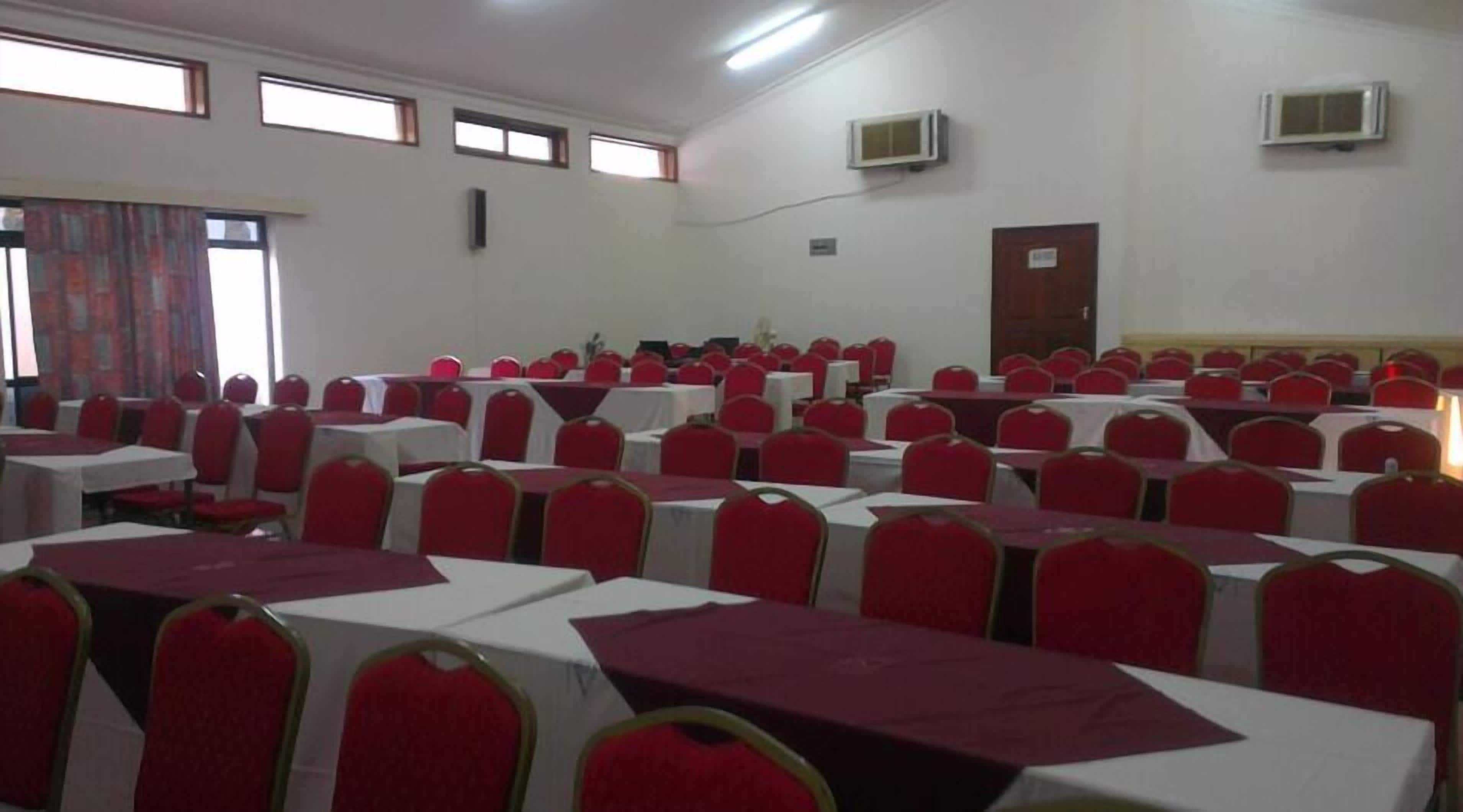 A conference room with rows of tables and chairs, air conditioning units, and a door.