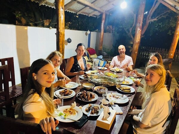 Un grupo de personas cenando en una mesa al aire libre con varios platos.