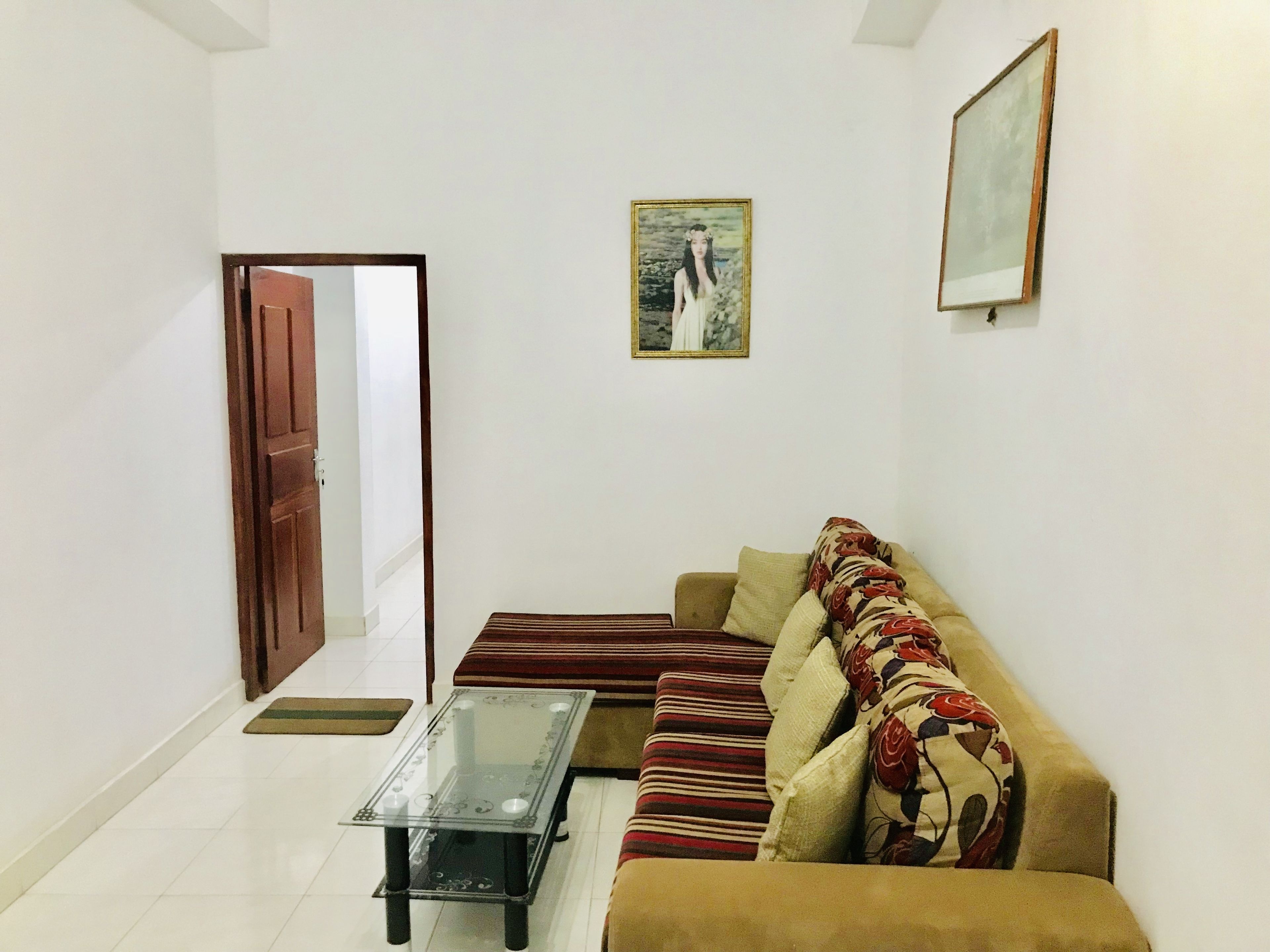 Una sala de estar con un sofá, una mesa de centro de vidrio, una puerta y un cuadro en la pared.