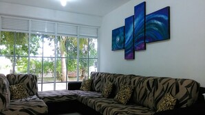 A living room with a sectional sofa, a large window with blinds, and a wall-mounted abstract painting.
