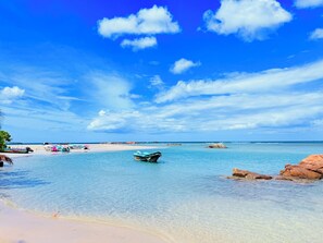 Una playa con agua turquesa cristalina, un bote y afloramientos rocosos.