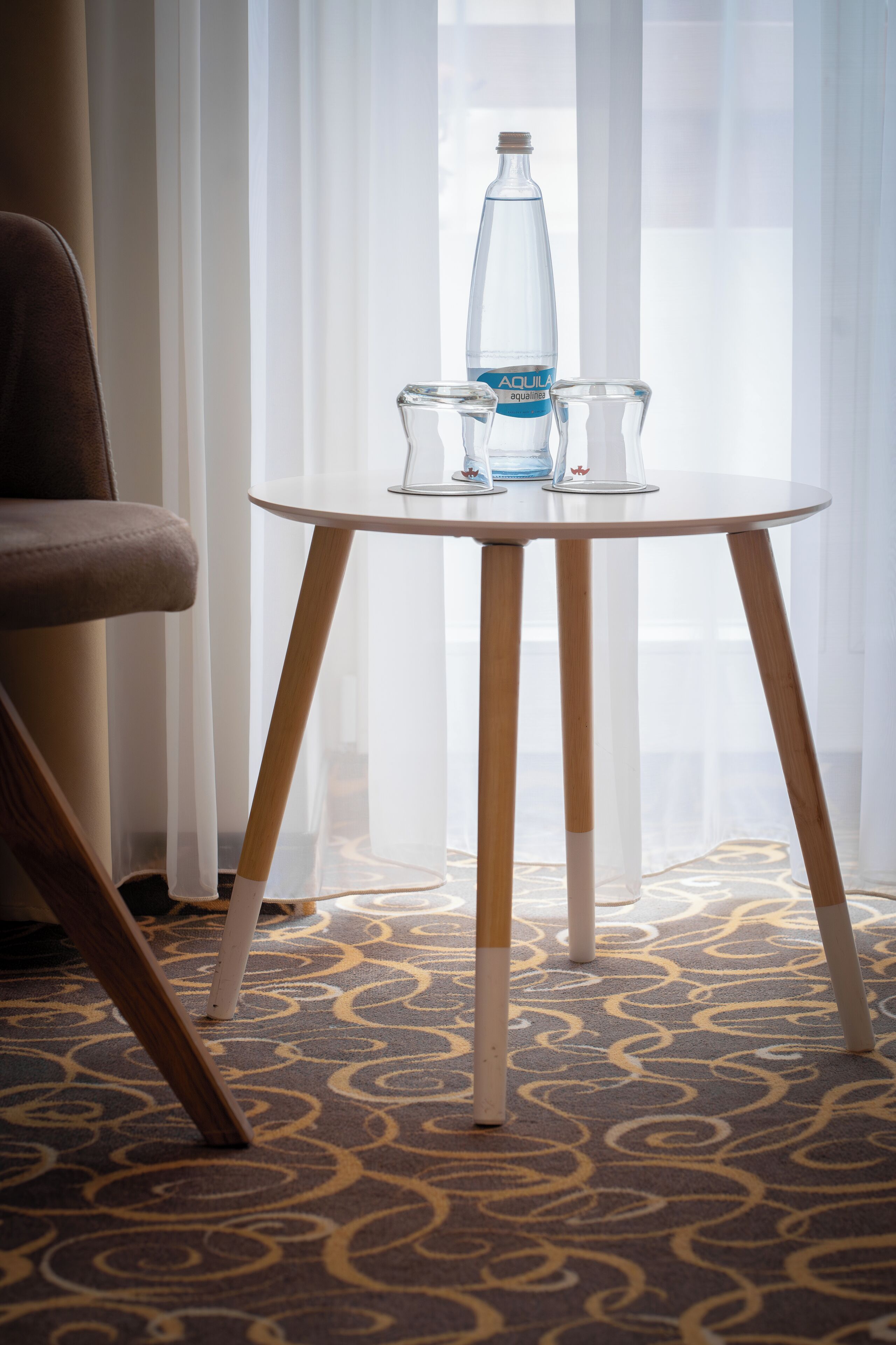 Une chambre d’hôtel avec une table ronde, une bouteille d’eau et deux verres.