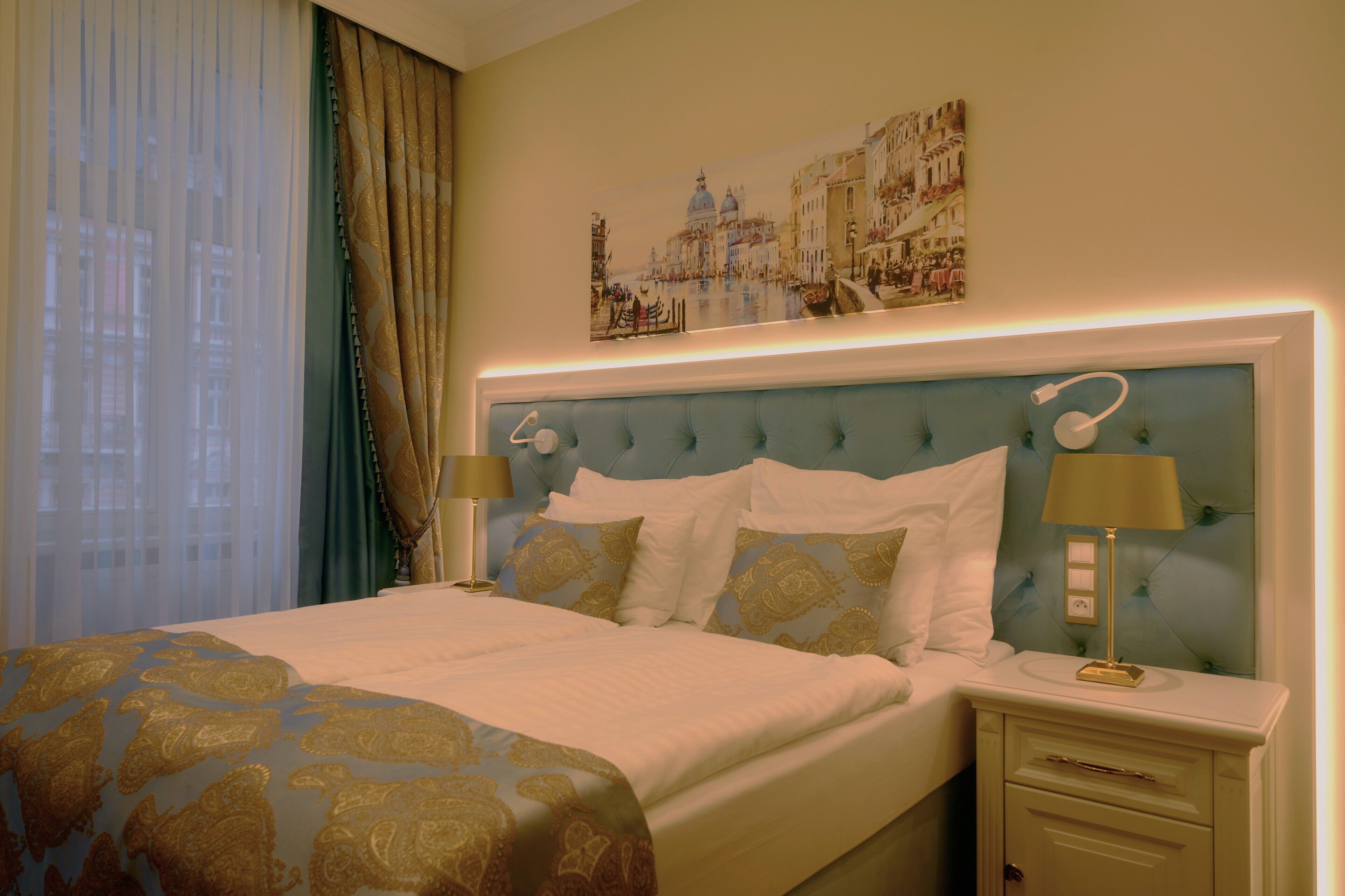 Una camera d'albergo con un letto, comodini, una lampada, un quadro appeso e una finestra con tende.
