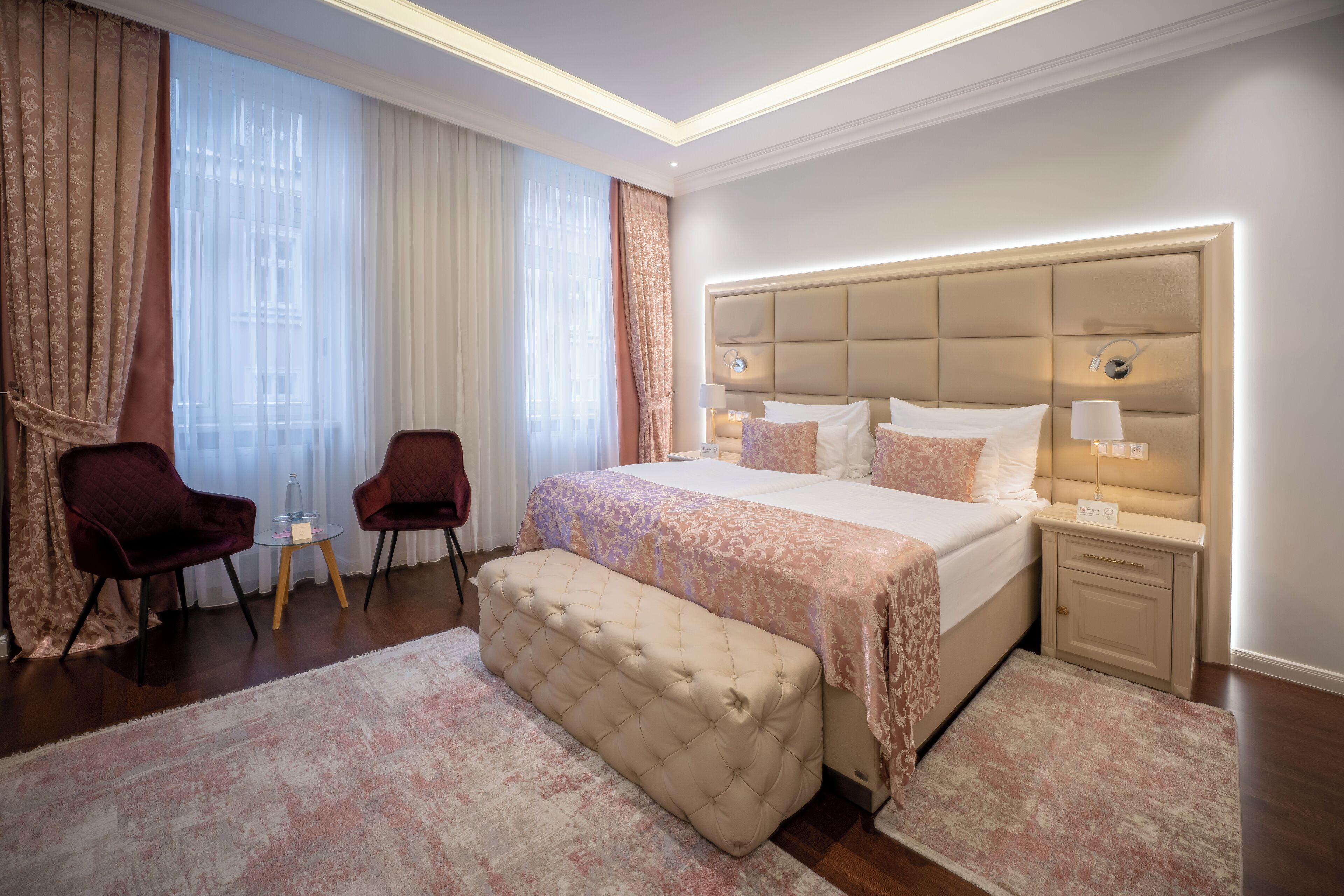 A hotel room with a large bed, two bedside tables, a bench, and a small table with a chair.