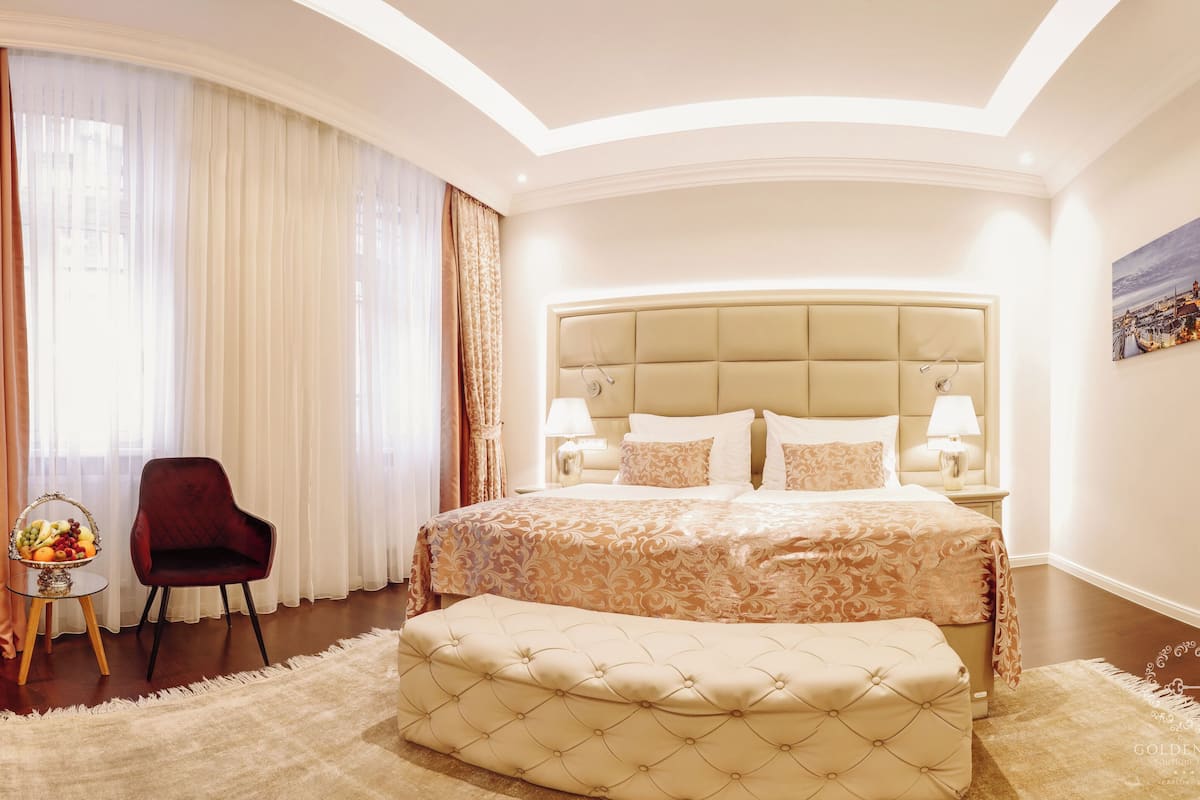 Habitación de hotel con una cama grande, dos sillones, una mesita con fruta y un cuadro en la pared.