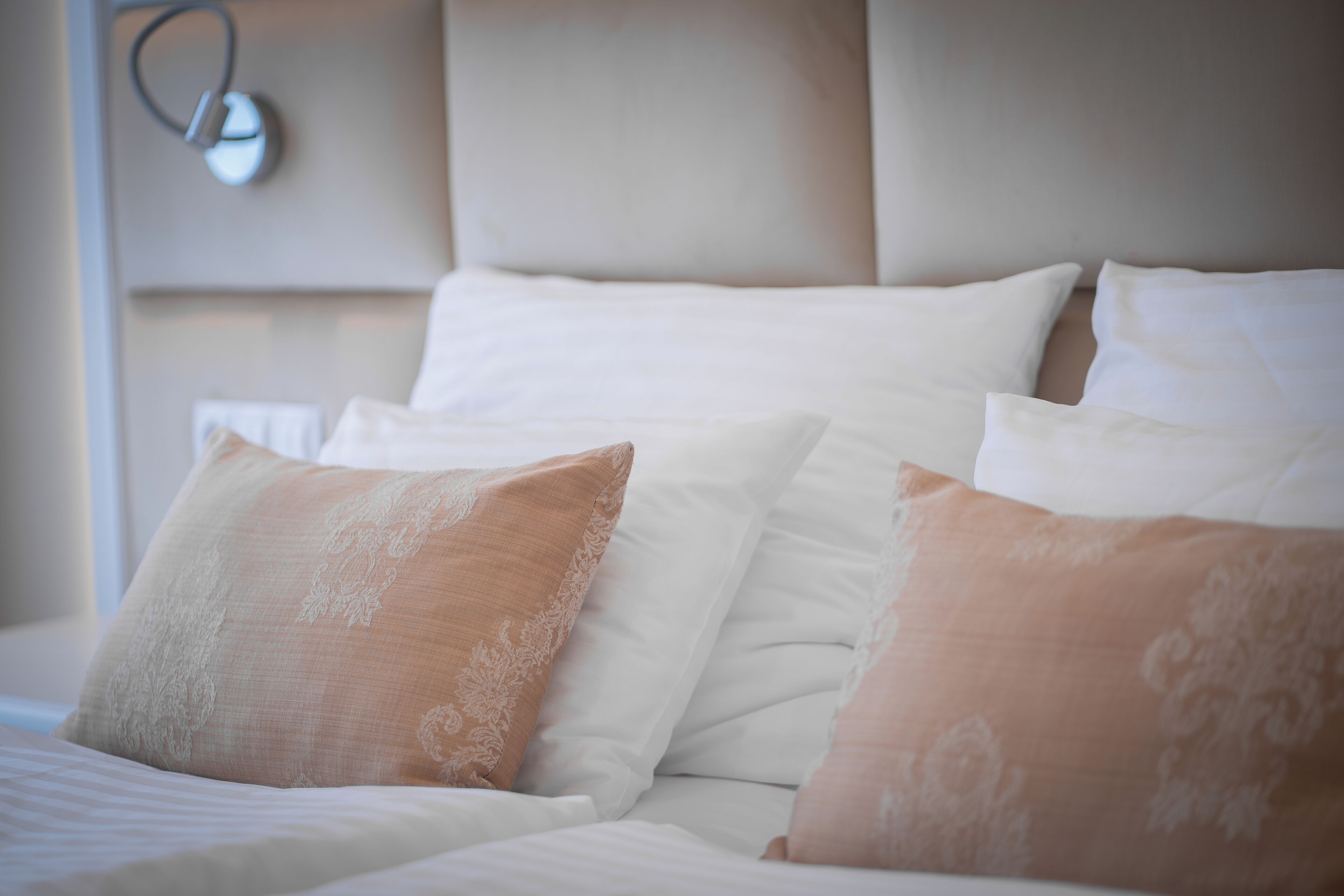 A neatly made bed with white and beige pillows, a headboard, and a bedside lamp.