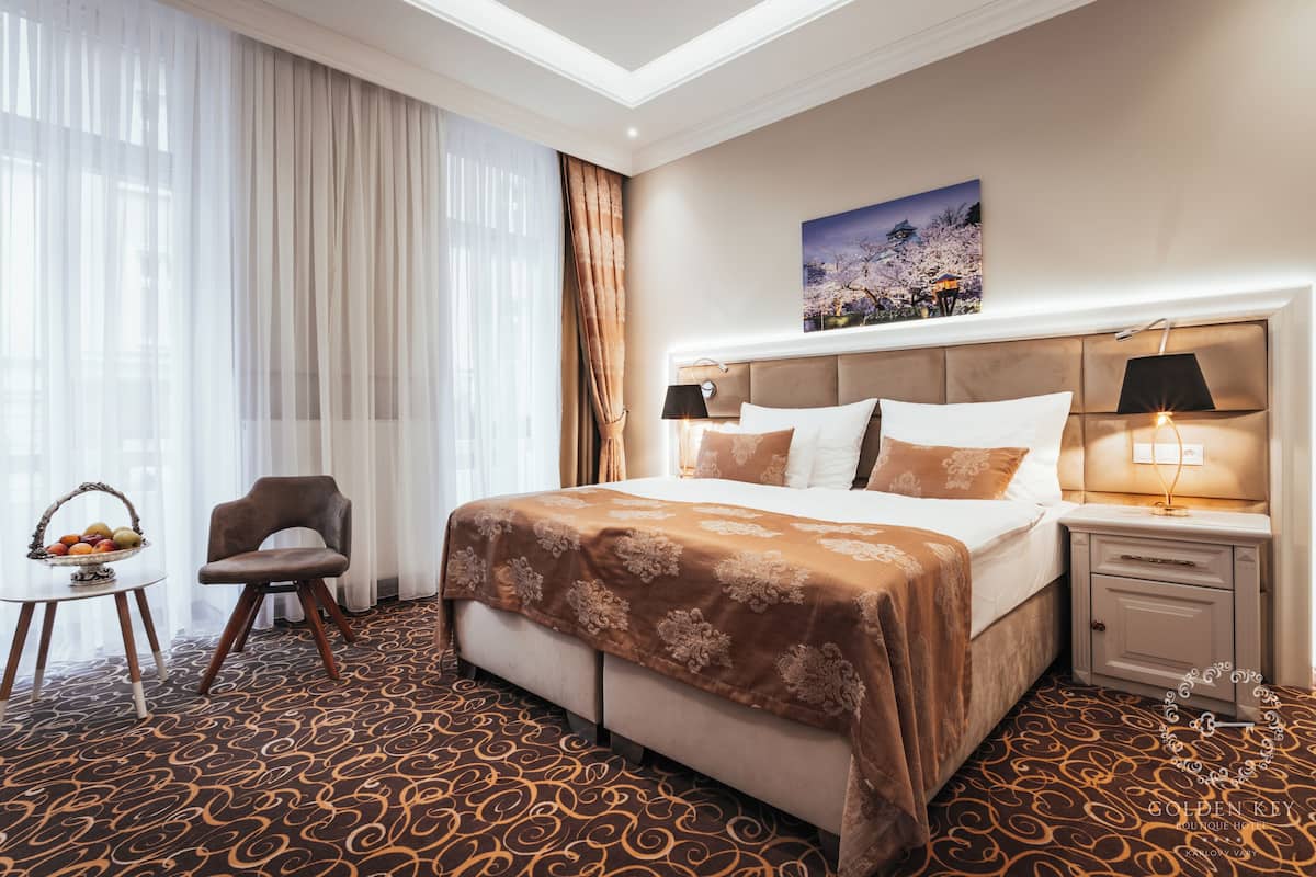 Habitación de hotel con una cama grande, una mesita de noche, una silla y una pequeña mesa con una cesta de fruta.