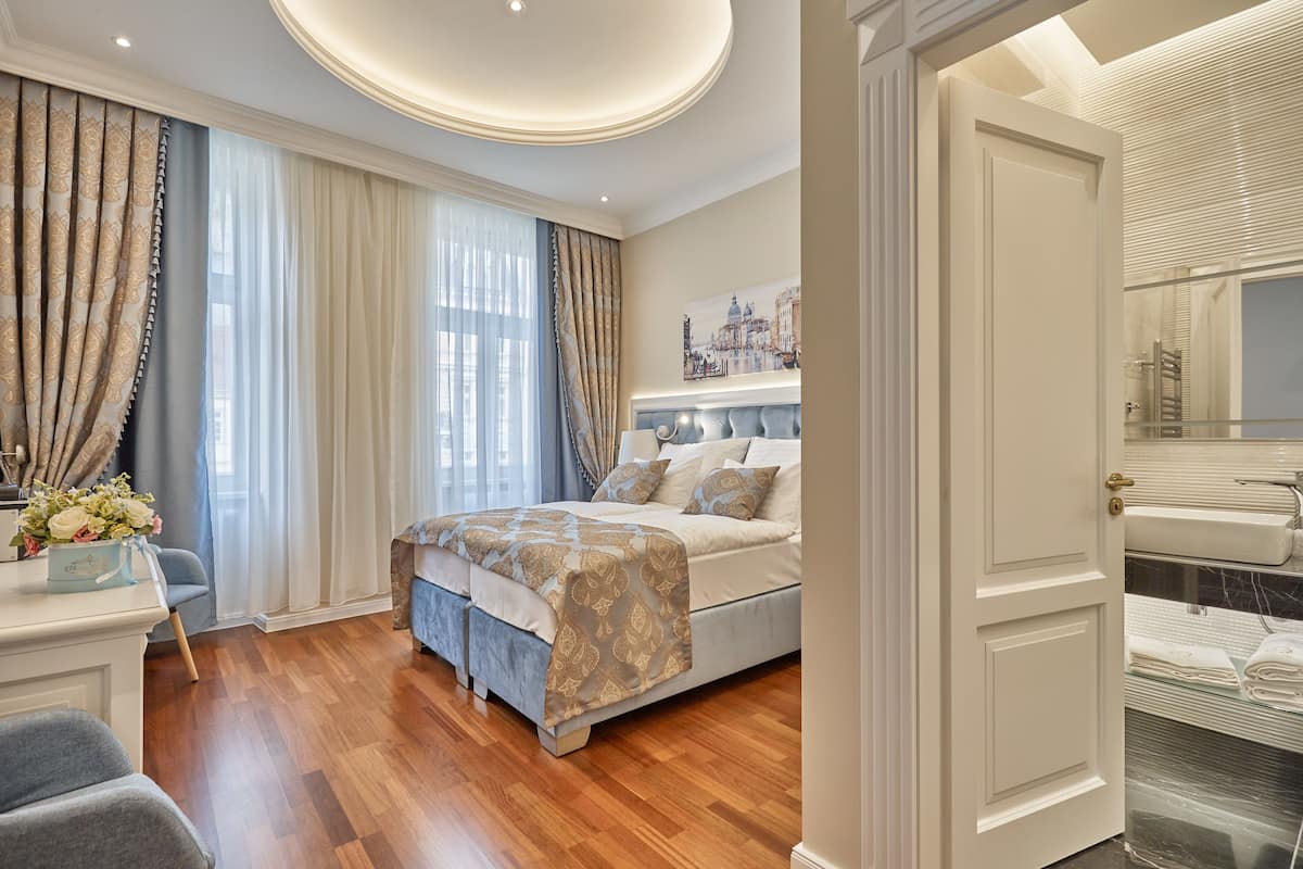 Un dormitorio con una cama grande, una mesita de noche con un florero y vistas al baño a través de una puerta abierta.
