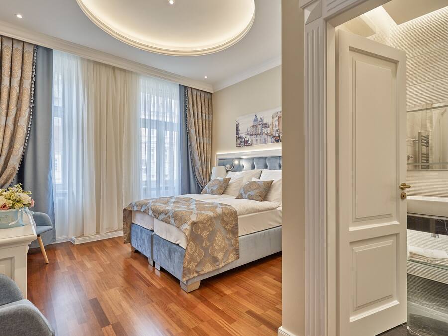 A bedroom with a large bed, a bedside table with a vase of flowers, and a view of the bathroom through an open door.
