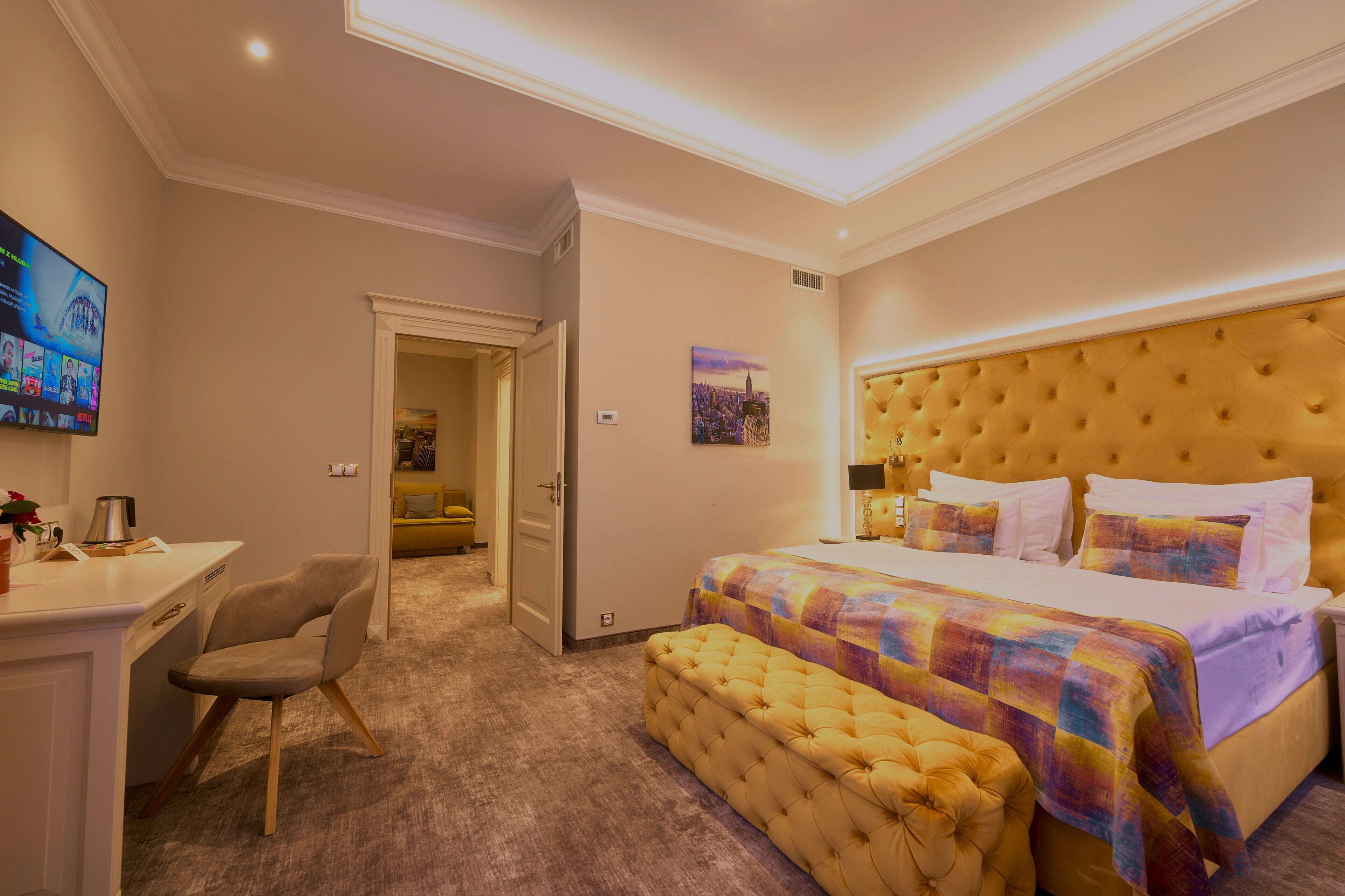 Een hotelkamer met een groot bed, een bureau en een stoel. Er is een televisie aan de muur en een schilderij.