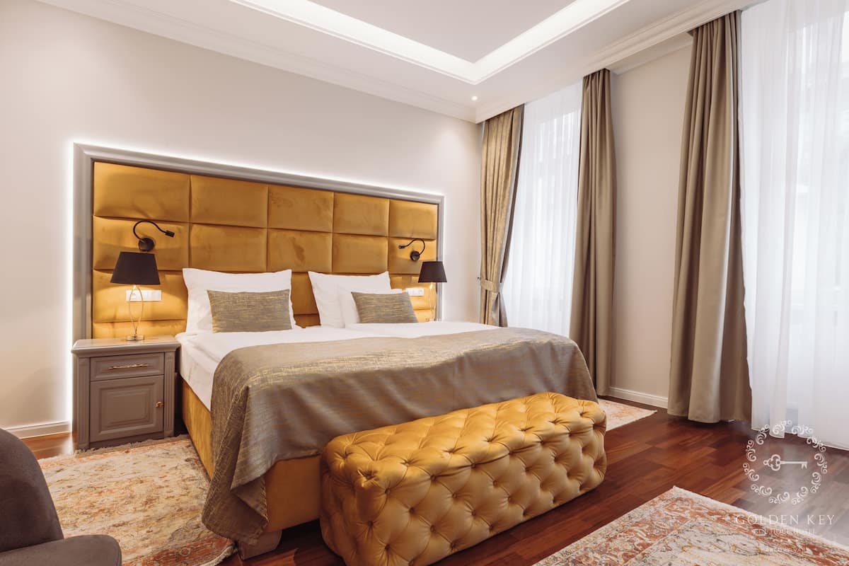 Un dormitorio con una cama grande, dos lámparas de noche, un banco capitonado y una mesita de noche.