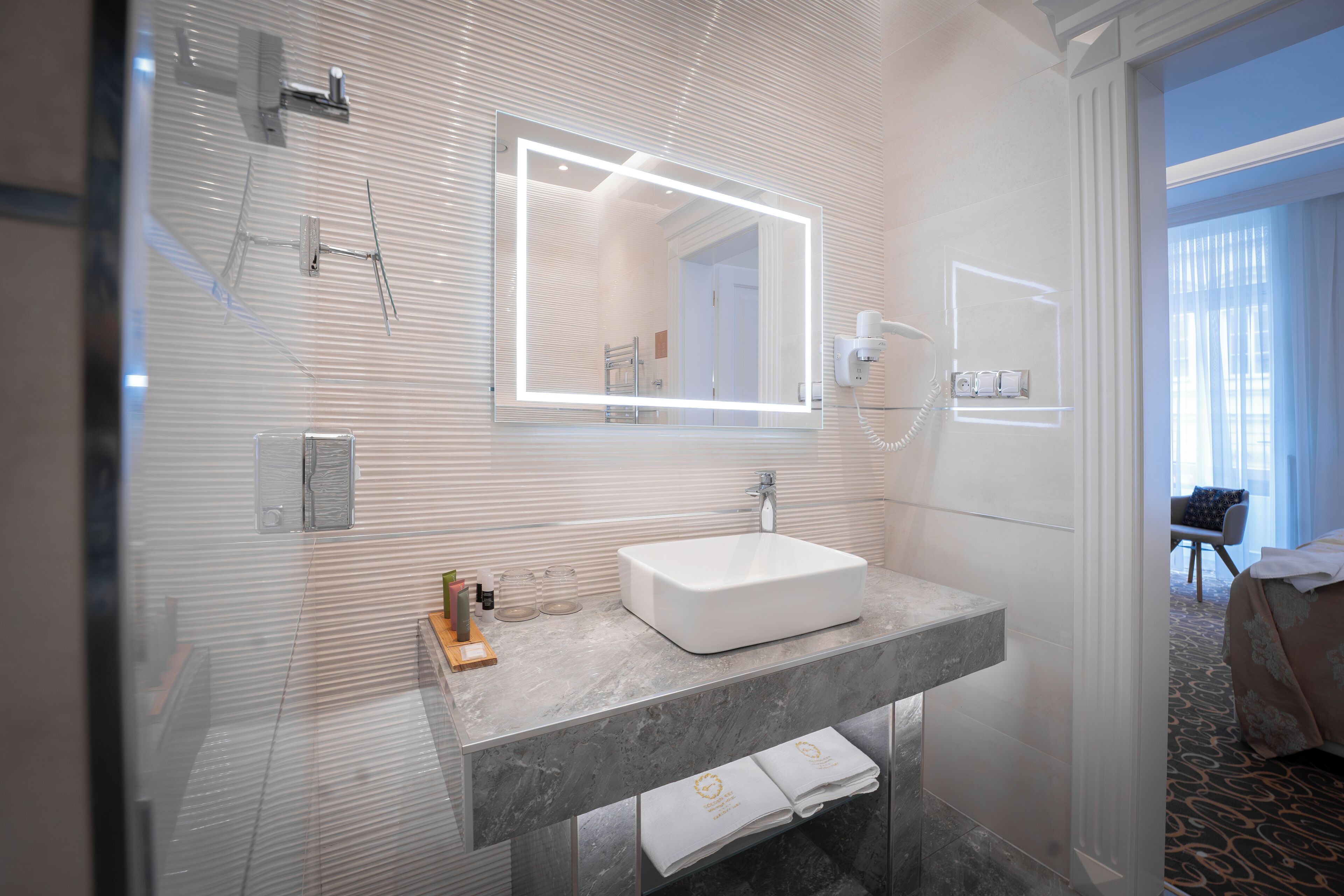 A modern bathroom with a large mirror, a white sink, and a towel rack.